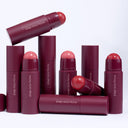 Several maroon-colored tubes of Too Much Attention - Stick Guance In Crema by Diego dalla Palma, arranged upright and lying down, with some caps removed to reveal rounded, blush-pink product inside—perfect for achieving un incarnato luminoso with their blush cremosa formula.