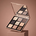The Nuda Essential - Palette Occhi, featuring nine highly pigmented nude eyeshadows, is open on a beige pedestal with its mirror reflecting the matching beige background.