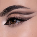 Primo piano di un occhio marrone con un deciso winged liner e un ombretto scuro e fumoso della Nuda Essential - Palette Occhi. Le sopracciglia folte e curate e l'angolo interno evidenziato utilizzano ombretti pigmentati per un look drammatico.