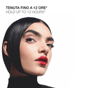 A woman with sleek, black, geometric hair and bold red lipstick poses against a white background, showcasing Mascara Ciglione volume for a defined look. Text above reads TENUTA FINO A 12 ORE HOLD UP TO 12 HOURS.
