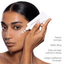 Una persona che applica dei puntini di Primer Perfezionatore Effetto Lifting da un tubetto sulle guance, accanto a un testo che elenca i benefici del prodotto in italiano.