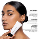 A woman holds a white tube of Primer Perfezionatore Effetto Lifting against her cheek next to text listing its ingredients: Niacinamide, Vitamin B3, and purified tapioca extract.