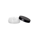 Un piccolo vasetto cosmetico trasparente e rotondo, con un coperchio nero a vite posto da parte, rivela l’interno vuoto: ideale per conservare Setseduce - Gel Fissante Professionale Per Sopracciglia e ottenere un effetto naturale.