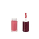 An open tube of Not So Innocent - Olio Gel Labbra lip gloss with a wand applicator. The frosted glass container is topped with a maroon cap featuring “Dear Dahlia” in white text. The applicator wand is coated with the pink gloss for labbra idratate and an effetto volumizzante.