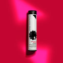 A white bottle of orgoglioriccio shampoo disciplinante modellante 100 ml stands upright on a vibrant pink background, casting a shadow. A black-and-white illustration of a curly-haired woman emphasizes its claim for capelli definiti.