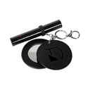 The Charm specchietto by Diego dalla Palma, a round black keychain mirror with a metallic D logo, is displayed open beside a black cylindrical item labeled CIGLIONE. Both feature stylish metallic accents.