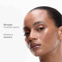 A person with dewy, glowing skin looks at the camera against a white background, highlighting the results of using the Hydrate Please Kit - Routine Viso Edizione Limitata. Italian text on the left reads: Risveglia l’incarnato spento and Idratazione intensiva.