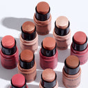 Several cylindrical sticks of ALL IN ONE - BLUSH in various shades are arranged in rows on a white surface, with some caps off to display the makeup viso products inside.