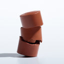 Three pieces of milk chocolate are stacked vertically, with the middle piece split to reveal its inner texture—evoking the way the ALL IN ONE - BRONZER  CONTOUR unveils its rich, blendable layers when used for sculpting. The chocolates balance elegantly on a white surface with a soft shadow, mirroring how carefully applied ALL IN ONE - BRONZER  CONTOUR enhances natural beauty.
