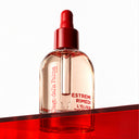Estremirimedi l’elisir Kit clear glass dropper bottle filled with pink multiazione hair oil, featuring a red cap and red branding text, resting on a red translucent surface.