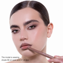 Una donna con capelli scuri e sopracciglia folte indossa un trucco marrone tenue creato con FULLFACE SLIM STICK - Matita multiuso in stick viso-occhi-labbra. Tiene la matita vicino alle labbra. La tonalità 86 è sugli occhi; la tonalità 81 sulle labbra.