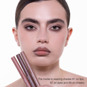 Una modella con eleganti capelli scuri indossa FULLFACE SLIM STICK - Matita multiuso nelle tonalità 81 sulle labbra, 87 sugli occhi e 89 sulle guance per labbra lucide, sopracciglia definite e trucco neutro, il tutto in una formula a lunga durata.
