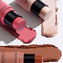 Tre stick di trucco ALL IN ONE - HIGHLIGHTER — composti da un fard rosa, un illuminante brillante e un bronzer marrone — sono disposti su uno sfondo chiaro, ciascuno con campioni di colore abbinati stesi in diagonale sotto di essi.