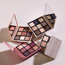 Tre Nuda Essential - Palette Occhi con specchietto incorporato poggiano su una superficie leggera, ognuna delle quali offre ombretti riccamente pigmentati nei toni del rosa, del nude, dell'oro e dello scuro, disposti in una griglia per infiniti look versatili.